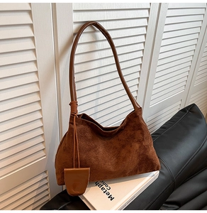 Brown suede hobo bag with dark leather handle and side charm detail on art book