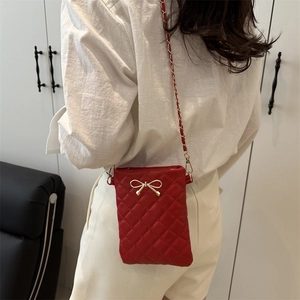 Sac bandoulière matelassé rouge avec nœud doré porté par un mannequin de profil