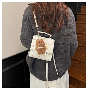 Close-up of white crossbody bag with cartoon bear patterns and plush bear charm