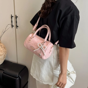 Pink textured pillow bag with pearl bow charm and gold hardware shown on a shoulder