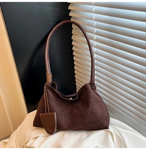 Close-up of a dark brown suede underarm bag featuring decorative rope and leather pendant
