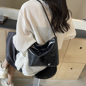 Minimalist black glossy bucket shoulder bag with bow detail worn by female model