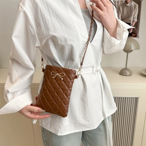 Brown quilted crossbody bag with gold bow accent and chain strap worn by a model