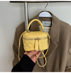 Detail of yellow quilted mini bag with golden double zippers and chain strap