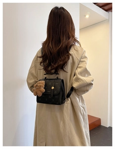 Back view of a black lychee texture backpack with bear print and plush pendant on a model