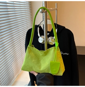 Lime green suede baguette bag with leather charm hanging on a modern display rack