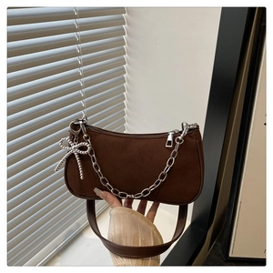 Détail d'un sac porté épaule en daim marron avec chaîne argentée et pendentif papillon