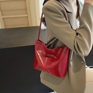 Chic red patent leather bucket bag with bow detail worn as an underarm shoulder bag
