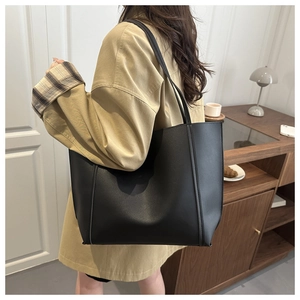 Large black matte tote bag styled with khaki trench coat in a warm interior setting