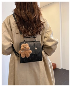 Detail of black pebbled leather backpack with rabbit print and plush bear charm on a trench coat