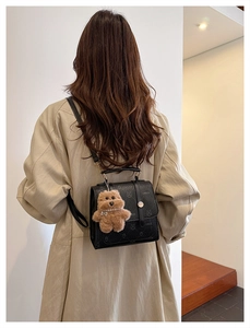 Detail of minimalist black pebbled leather backpack with cute teddy bear plush charm
