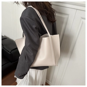 Detail view of large beige leather tote bag with thin dual shoulder straps on a model