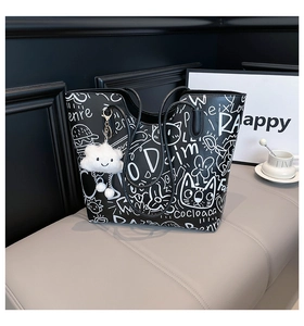Detail of graffiti tote bag featuring white doodles and a cloud charm on black PU leather