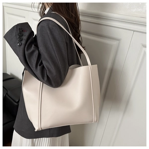 Minimalist beige leather tote bag with slim shoulder straps shown in a chic lifestyle setting