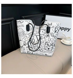 Detailed view of the white leather tote bag featuring artistic black graffiti and rope handles