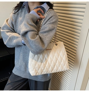Close-up of white quilted tote bag with gold logo and elegant chain strap detail