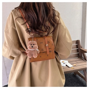 Detail of a brown leather backpack with bear prints and a plush charm in a scenic outdoor setting
