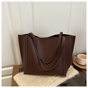 Close-up of deep brown leather tote bag with long double handles on a plush mat