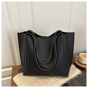 Detail of a black matte leather tote bag with vertical piping and long handles for shoulder use