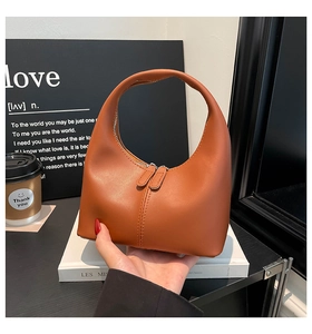 Close-up of a brown moon-shaped handbag with dual zippers held in a lifestyle setting