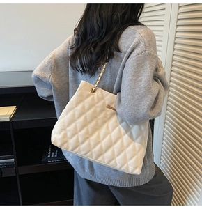 Detail of a beige quilted crossbody bag with golden chain strap worn by a female model
