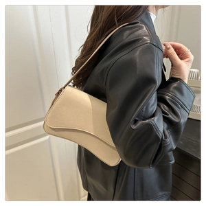 Detail of minimalist cream leather underarm bag with curved flap on shoulder