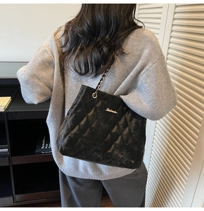 Detail of black quilted shoulder bag with gold chain strap shown on model's shoulder