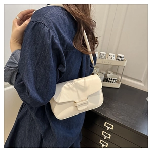 Détail du sac à bandoulière crème avec chaîne dorée porté sur une chemise en denim