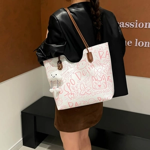 White tote bag with pink graffiti patterns and brown leather straps including a plush charm