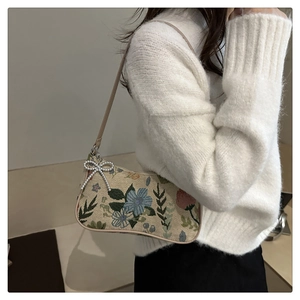 Detail of floral embroidery underarm bag with silver bow charm and thin leather strap