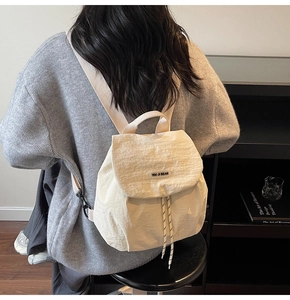 Close-up of cream white nylon mini backpack with drawstring and flap closure detail