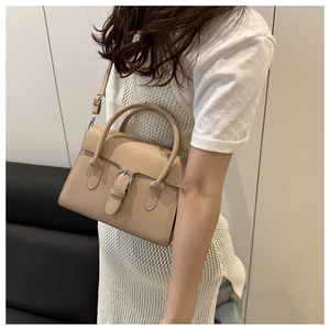 Detail of a beige trapezoid crossbody bag with metallic buckle and round handle