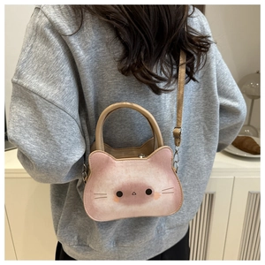 Sac à bandoulière chat rose en peluche porté sur un manteau blanc dans un décor intérieur