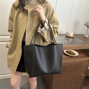 Minimalist large black leather tote bag with long handles shown in a lifestyle setting