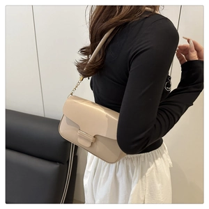 Détail d'un sac à rabat beige rectangulaire avec bandoulière chaîne dorée sur un modèle