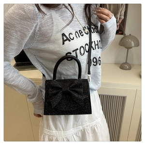 Detail of black sequin crossbody bag with a large bow shown on a model in a modern room