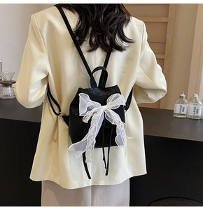Detail of mini black backpack featuring a large white lace bow and drawstring closure