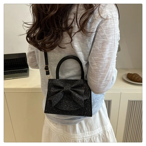 Close-up of black evening bag featuring a large glitter bow and versatile leather strap