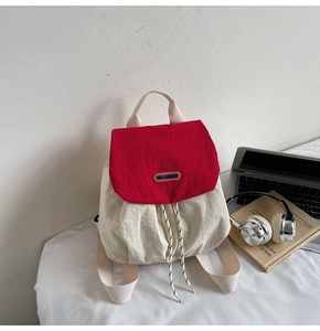 Detail of red and white nylon backpack featuring drawstring closure and logo patch
