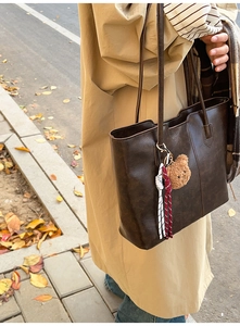 Detail of a dark brown vintage faux leather tote bag with a cute plush bear charm