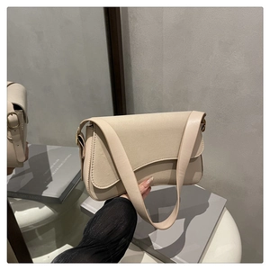 Detail shot of a cream leather crossbody bag with minimalist flap design and wide strap