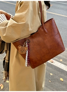 Detailed view of a vintage brown leather tote bag with a cute plush bear charm on its strap