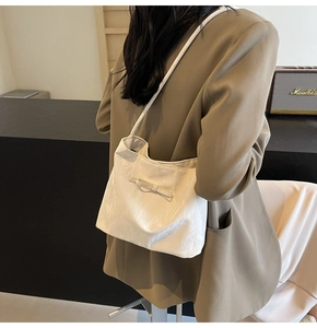 Détail du sac à bandoulière blanc plissé avec nœud sur un mannequin en blazer beige
