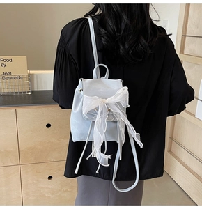 Detail of light blue mini backpack with large white lace bow shown on model's back
