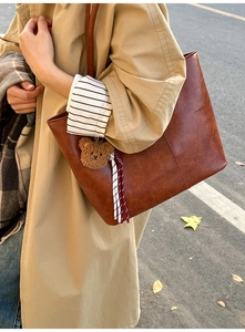 Detail of a brown textured tote bag with a cute plush bear charm and ribbon decor