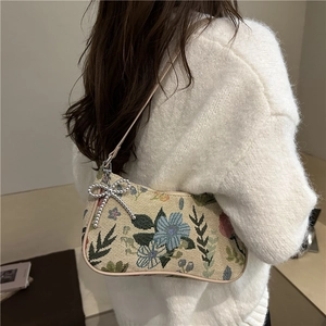 Retro floral tapestry underarm bag with silver bow charm worn by a model in warm light