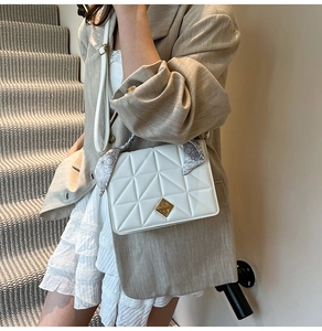 Gros plan sur le sac matelassé blanc avec fermoir doré et détail de foulard en soie sur l'anse