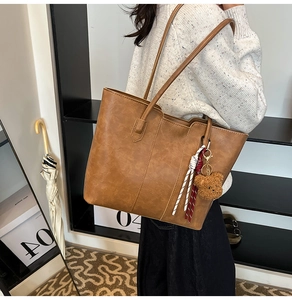 Detailed view of retro brown faux leather tote bag with plush bear charm on model