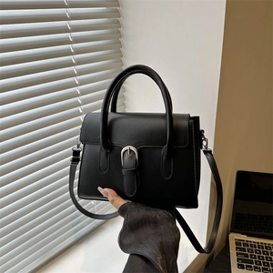 Close-up of black matte leather handbag with silver buckle held by hand for scale