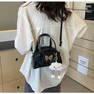 Détail du sac Boston noir avec ornement papillon doré et breloque nuage en peluche